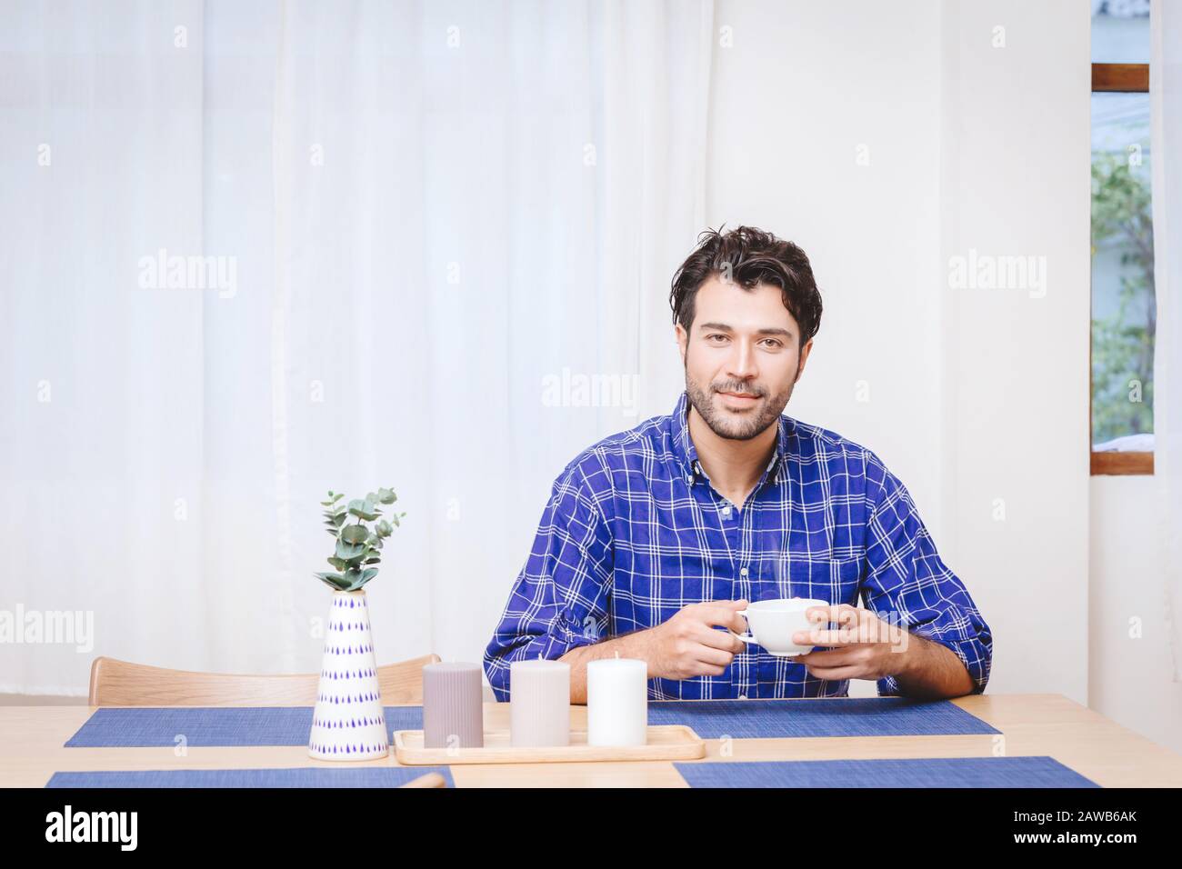 gentle handsome man sitting in the kitchen table to drink some hot beverage or coffee with white space for text. Stock Photo