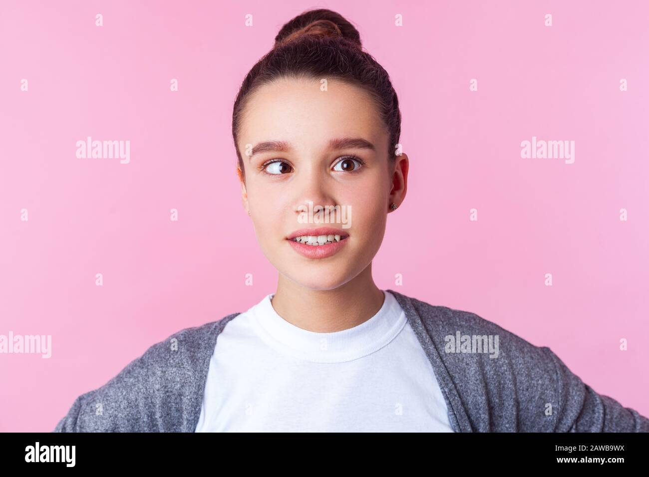 Portrait of adorable funny brunette teen girl with bun hairstyle in casual clothes fooling around with crossed eyes, having fun, childish positive fac Stock Photo