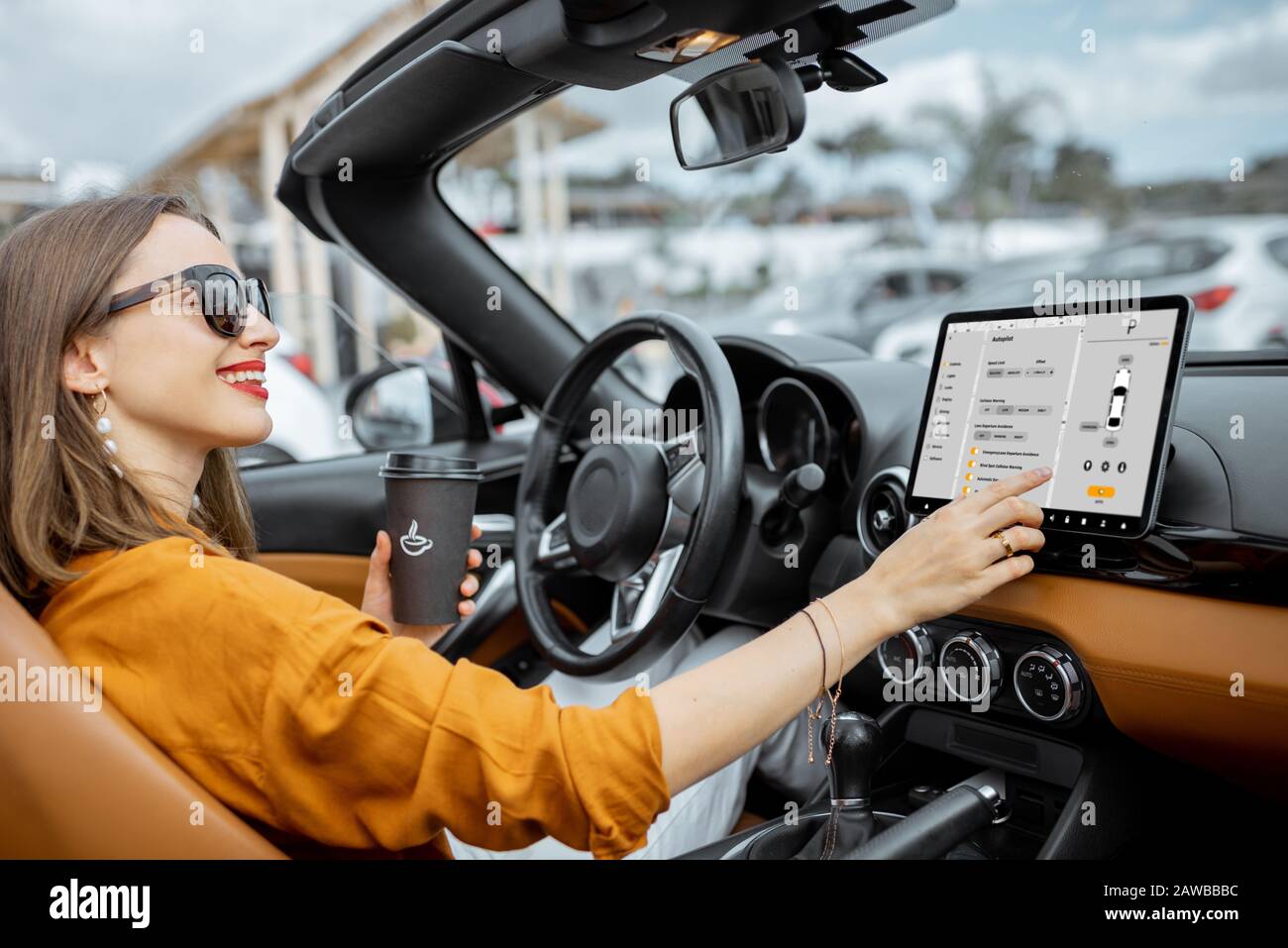 Cheerful woman controlling car with a digital dashboard, switching autopilot mode while driving a cabriolet. Smart car concept Stock Photo