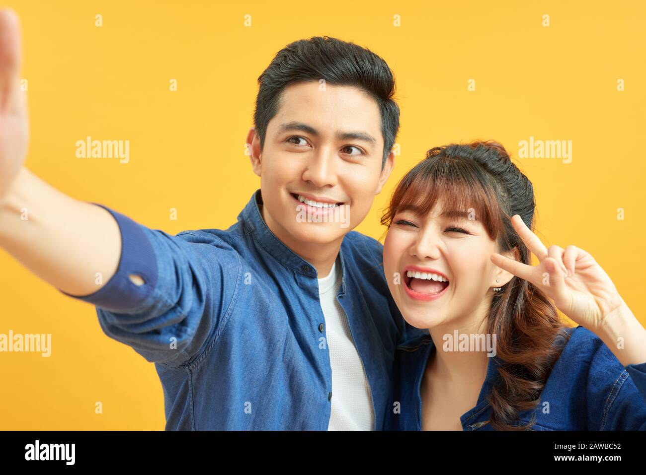 Self portrait of funny foolish cheerful adorable young cute couple smiling showing teeth, looking straight with opened mouths over yellow background, Stock Photo