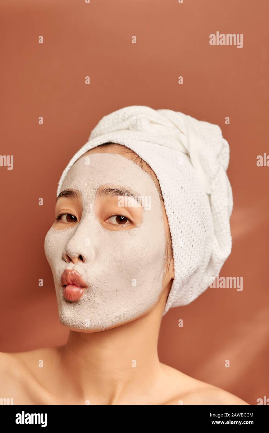 Beautiful Asian woman applying facial mask on her face. Skin care and treatment, spa, natural beauty and cosmetology concept. Stock Photo