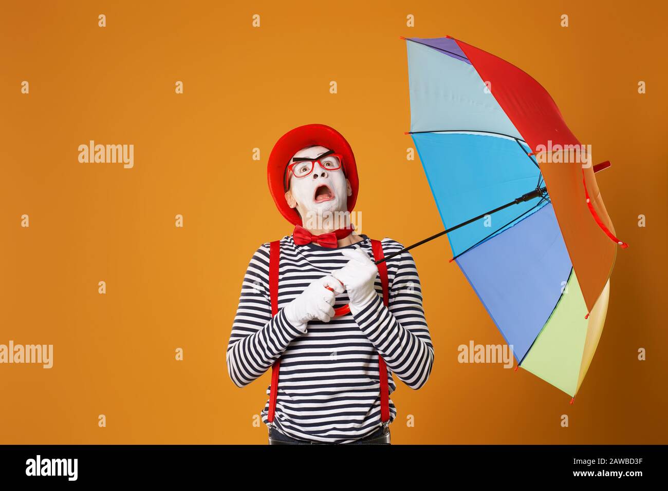 Mime looking up with multi-colored umbrella isolated on empty orange background in studio Stock Photo