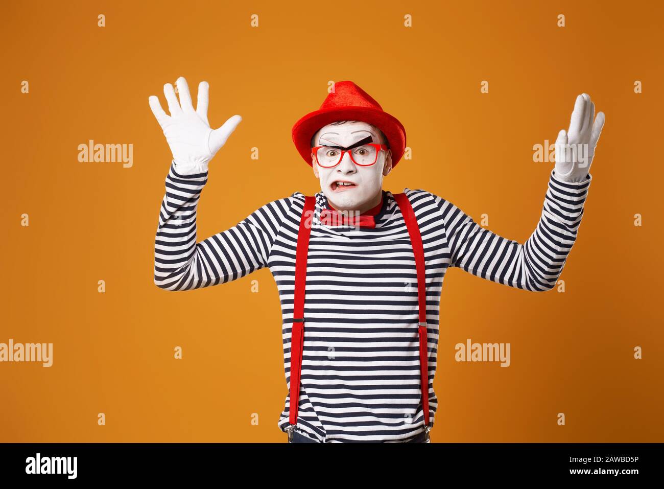 Sad mime clown in red hat and in vest with hands up on empty orange background Stock Photo
