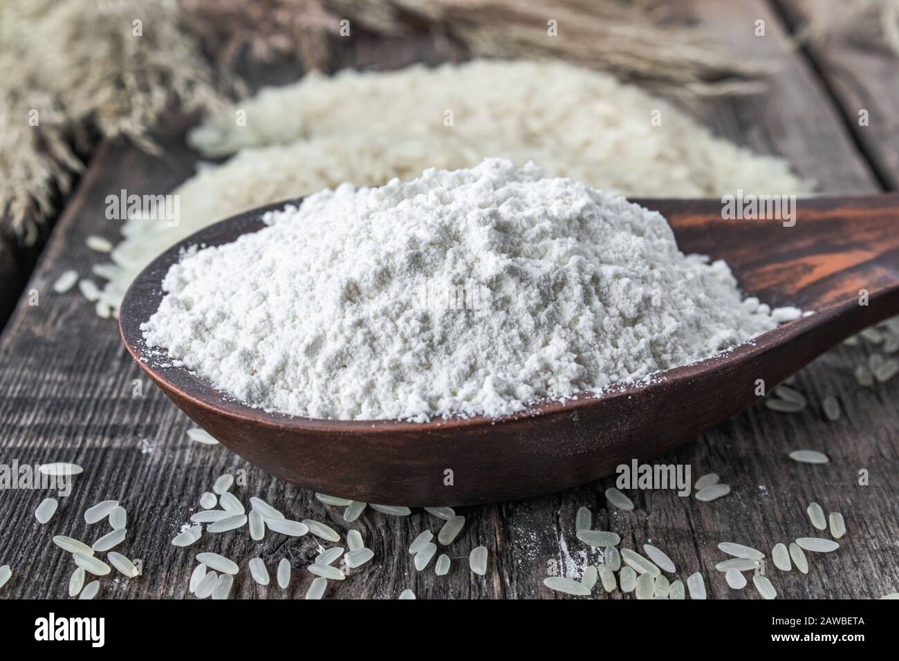 Rice flour in a spoon next to white rice on old boards. Jasmine rice