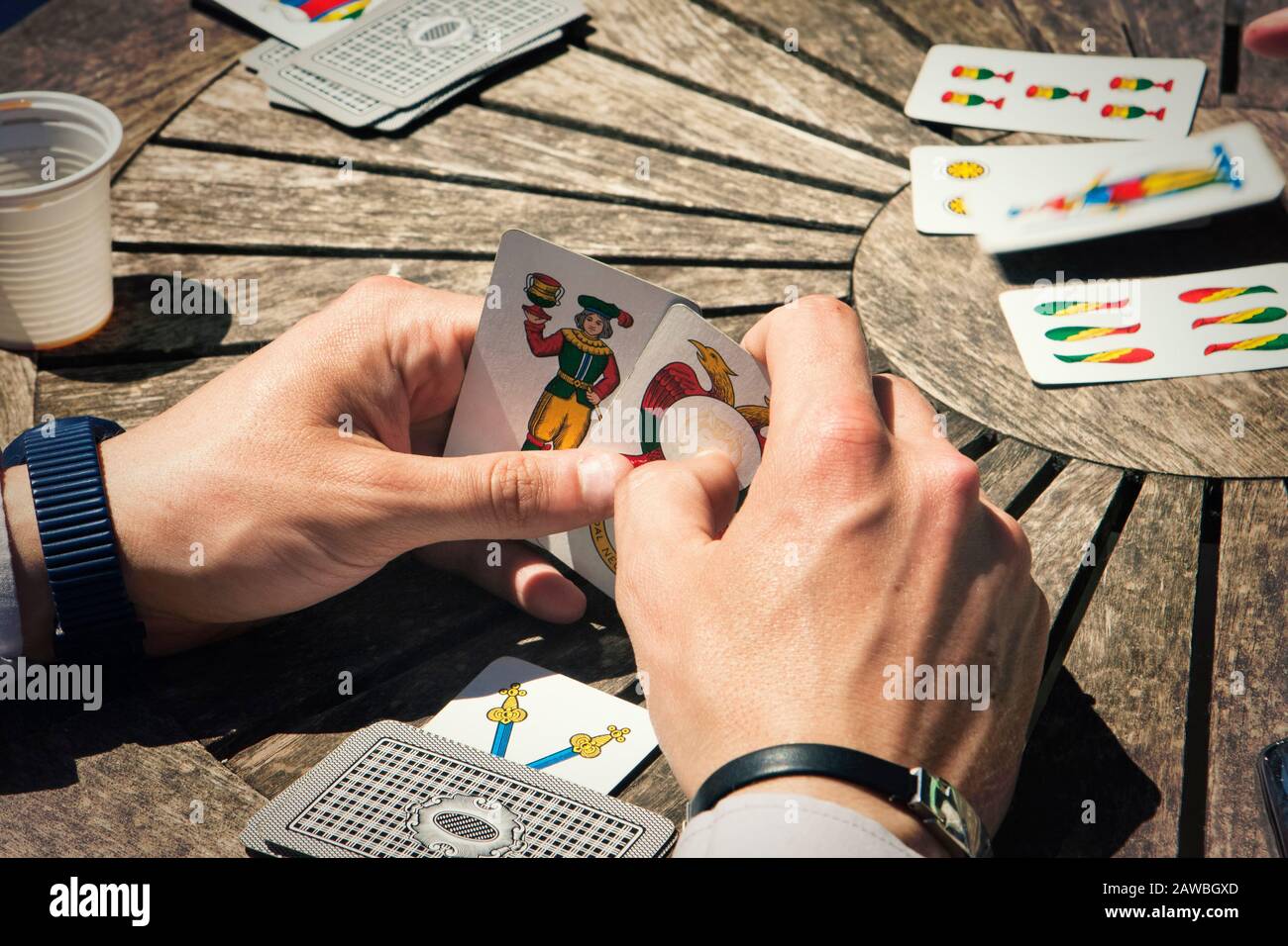 First person view of hands playing Trump cards with traditional Neapolitan cards on a circular wooden table Stock Photo