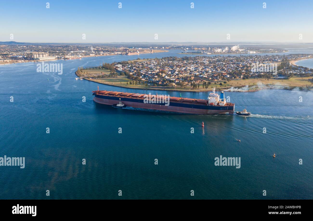 A coal ship is brought into port by tug boats in Newcastle NSW Australia. Newcastle is one of the busiest coal export ports in the world. Suburb of St Stock Photo
