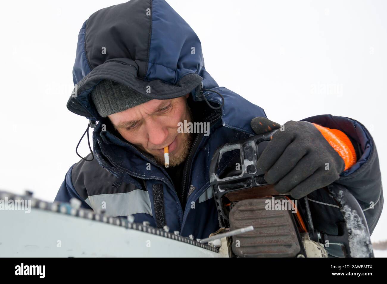 A worker in a blue jacket sharpens a chainsaw chain. Stock Photo