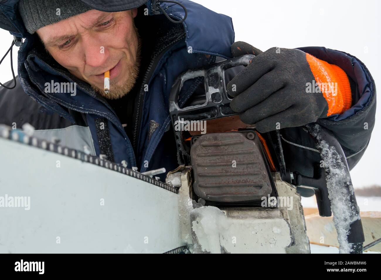 A worker in a blue jacket sharpens a chainsaw chain. Stock Photo