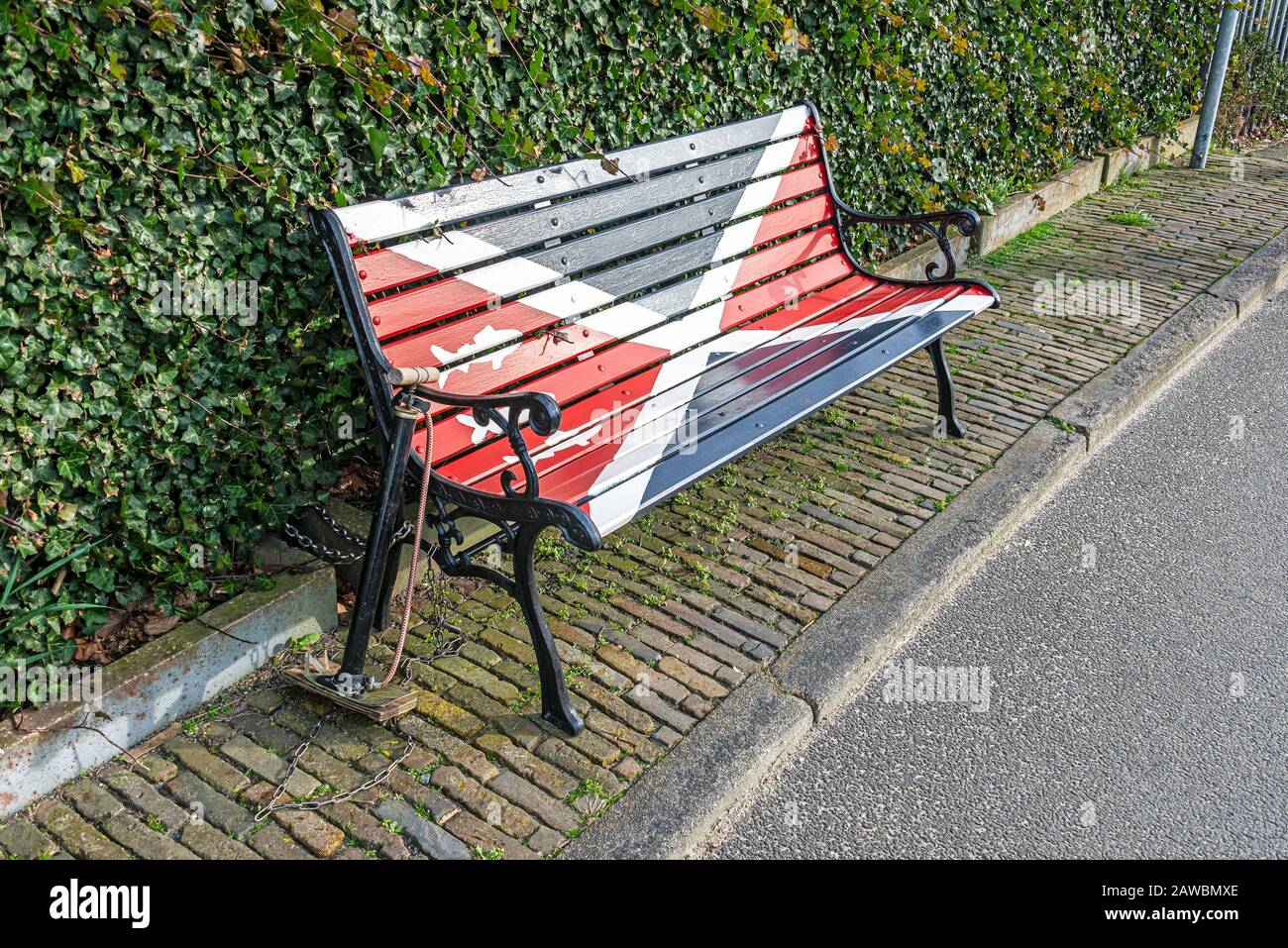 wooden garden bench with red blue and white planks standing on the street with a bicycle pump attached with a chain to the garden bench Stock Photo