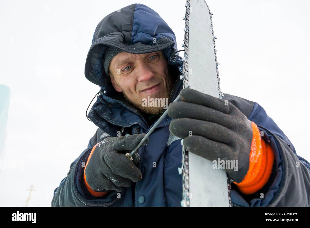 A worker in a blue jacket sharpens a chainsaw chain. Stock Photo