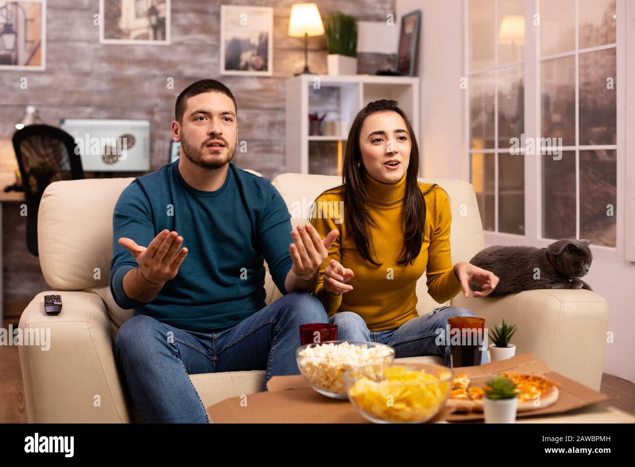 Couple cheering for their favourite team while watching TV and eating fast food Stock Photo