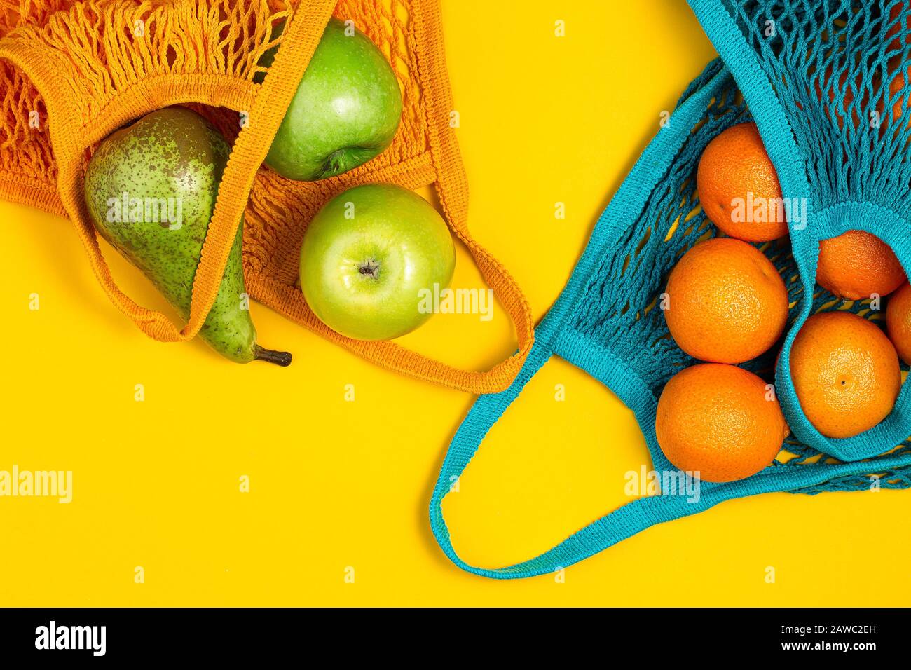 Tangerines and green apples in string bag on yellow background. Zero waste, plastic free concept. Healthy clean eating diet and detox. Summer fruits. Stock Photo