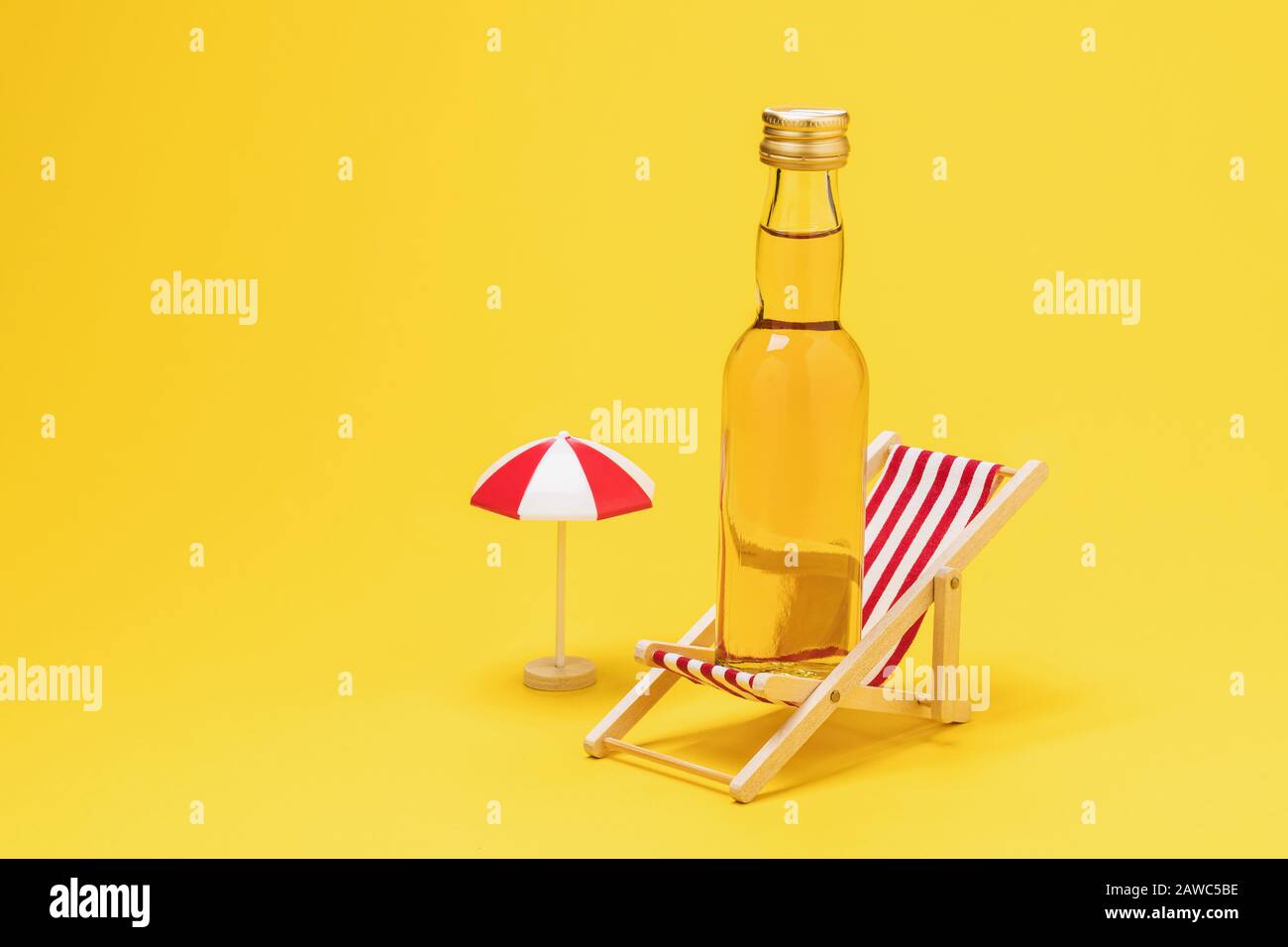 Bottle of whiskey and deck chair on a yellow background with copy space. Concept on the topic of alcohol abuse on the beach Stock Photo