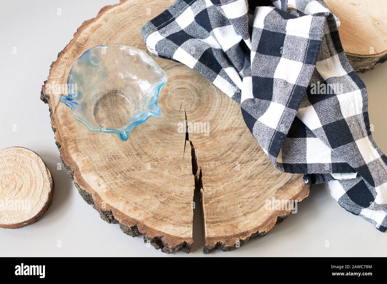 Wooden rounds decoration for serving food. Oak cutting board with a crack, glass bowl and checked black and white kitchen towel Stock Photo