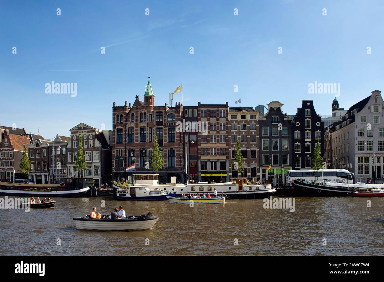 View of people riding open boats in Amstel river doing canal cruise tours. Historical, traditional and typical buildings are in the background. It is Stock Photo