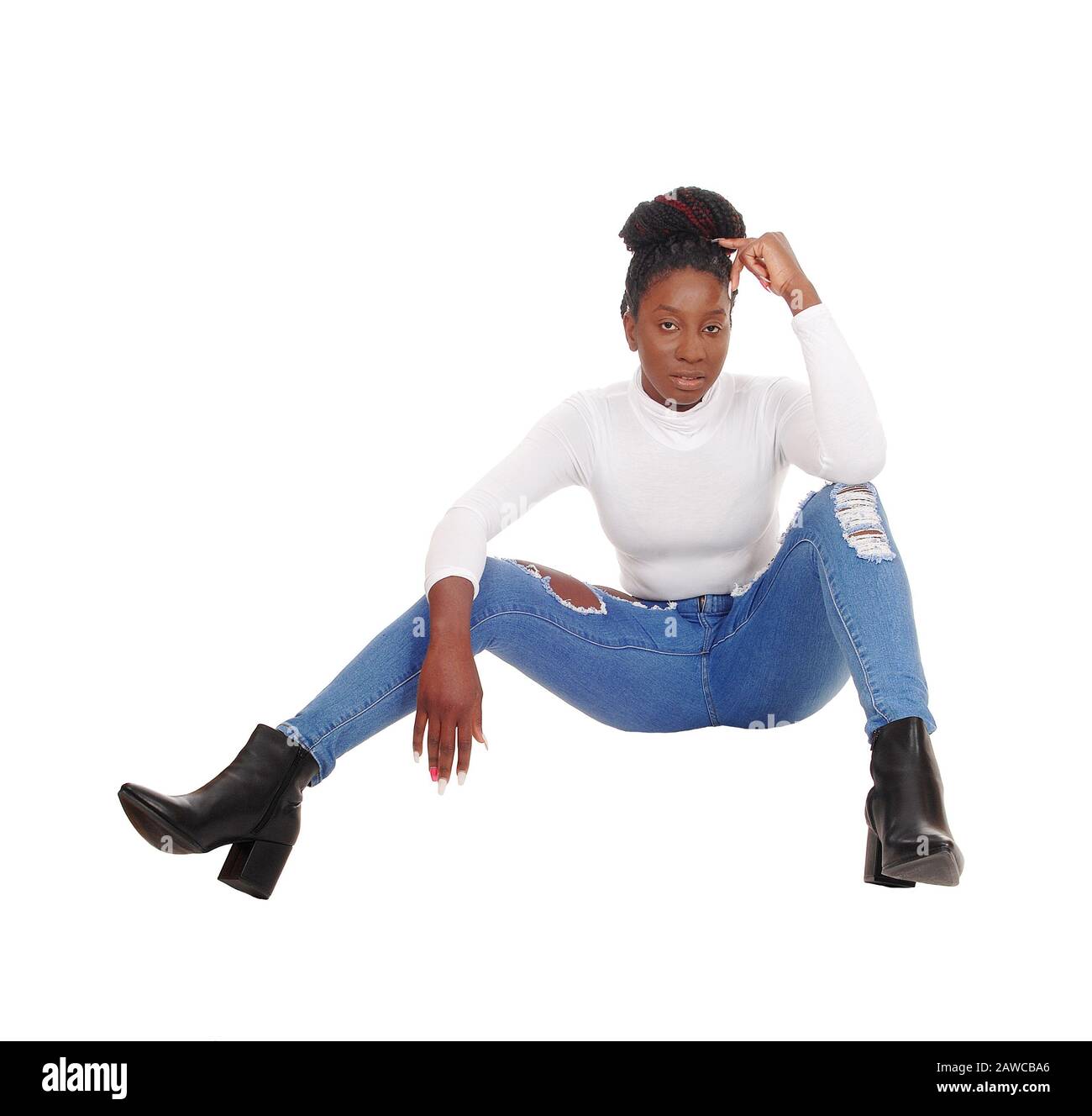 A beautiful tall African American woman sitting in jeans and white top on the floor in the studio, isolated for white background Stock Photo