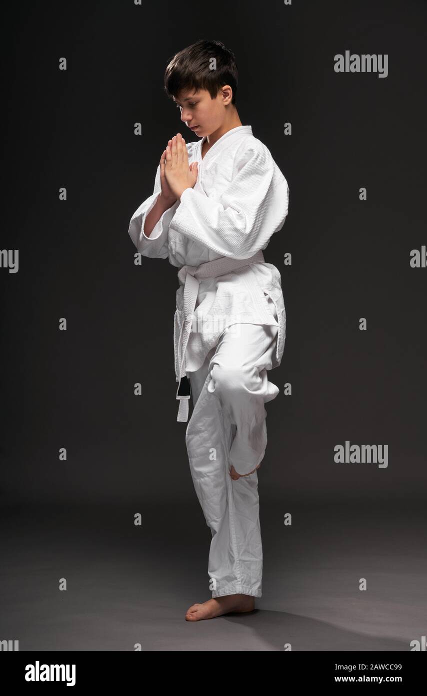 a teenager dressed in martial arts clothing poses on a dark gray