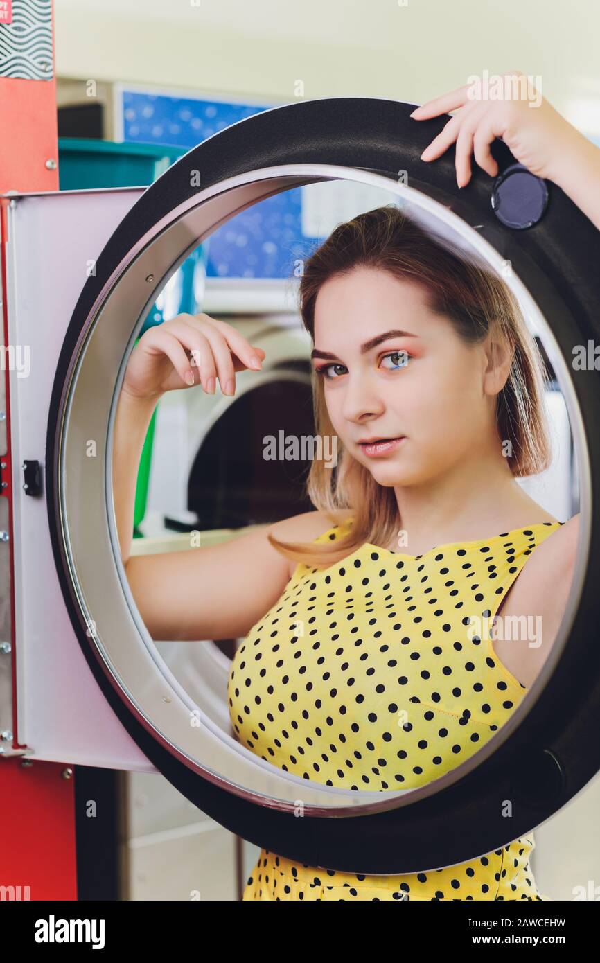 Beautiful young woman is sitting on the floor near washing machine Stock Photo
