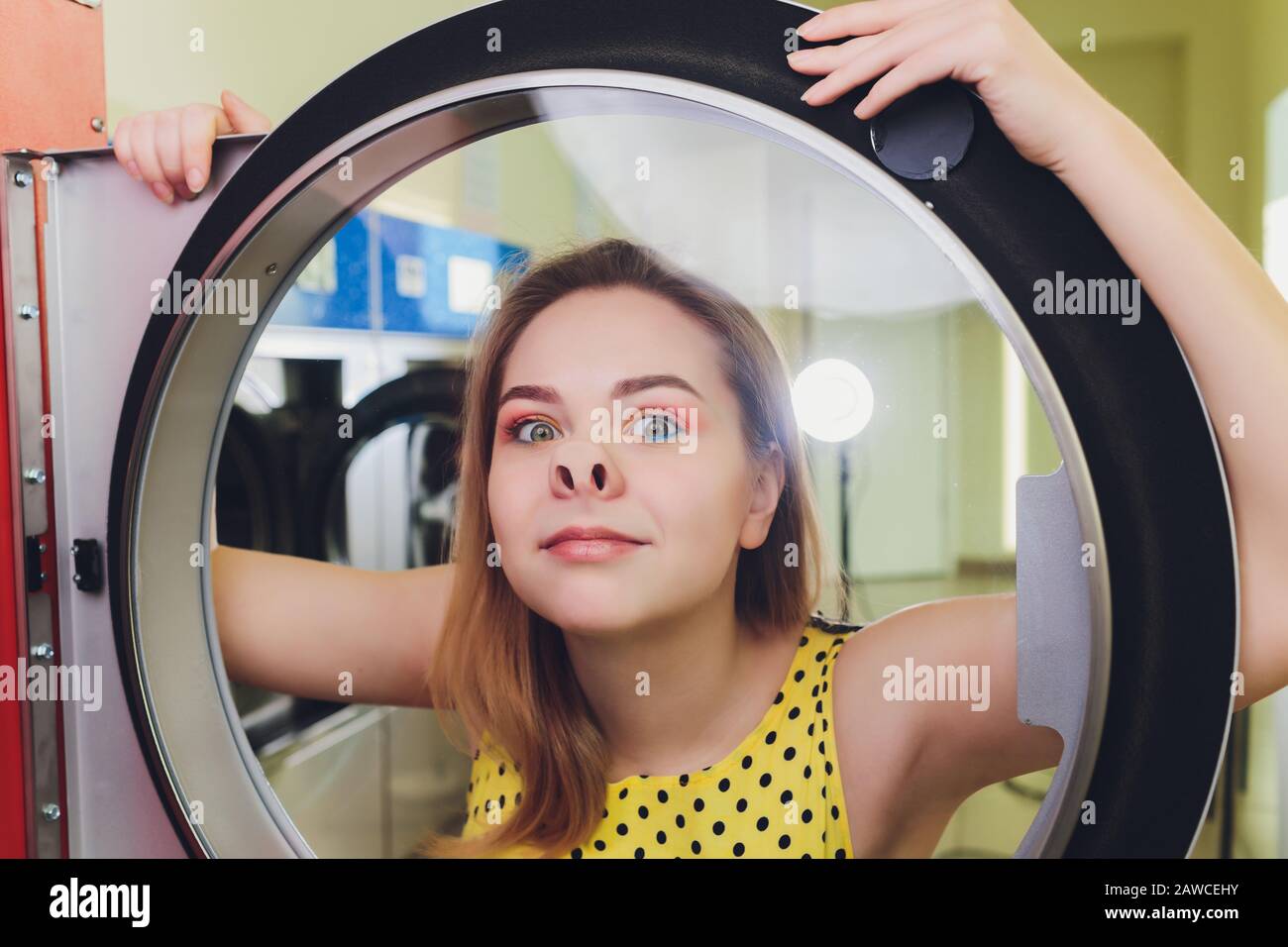 Beautiful young woman is sitting on the floor near washing machine Stock Photo