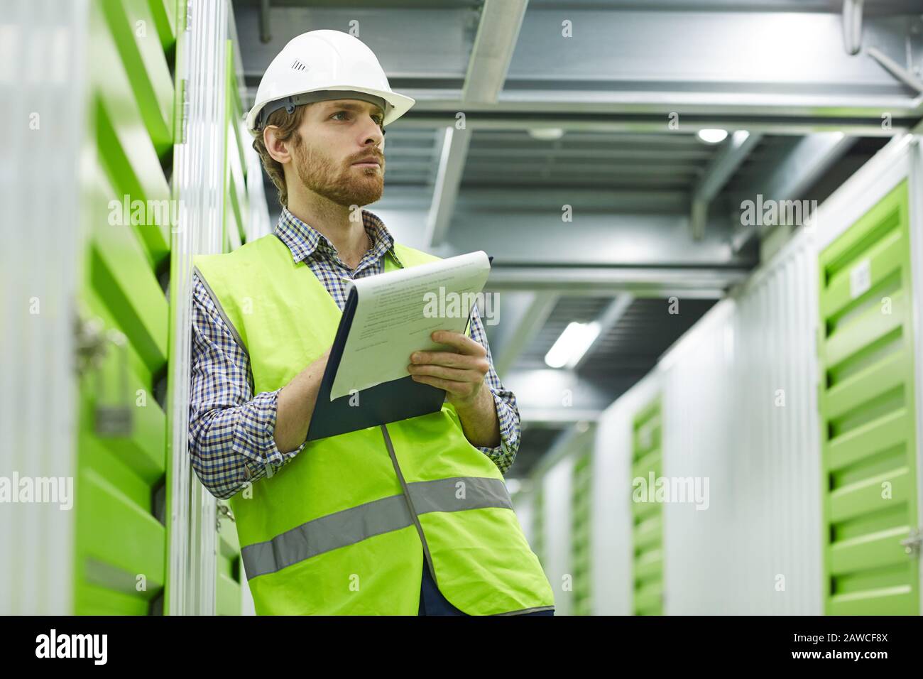Serious young manual worker in working clothing standing and working with documents in warehouse Stock Photo