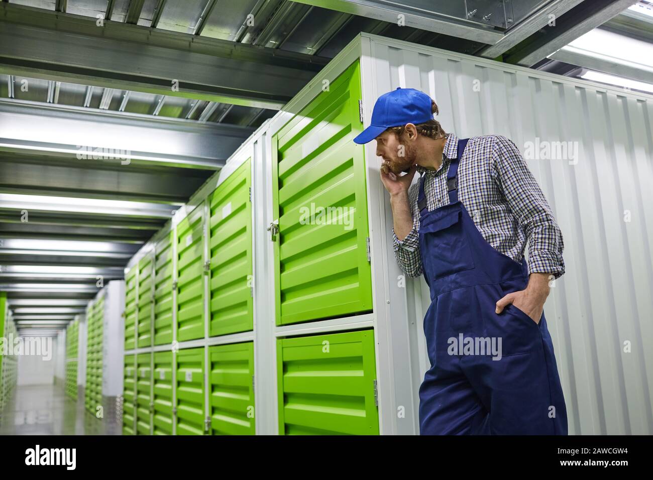 Young worker in overalls standing near the green boxes and waiting for ...