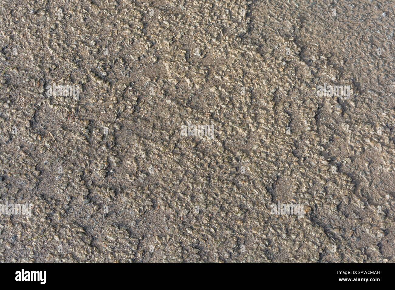 Side-lit rough surface of a rural country road (possibly ravelling) tarmac. For bumpy surface, rough ride, damaged, uneven surface, rough texture. Stock Photo