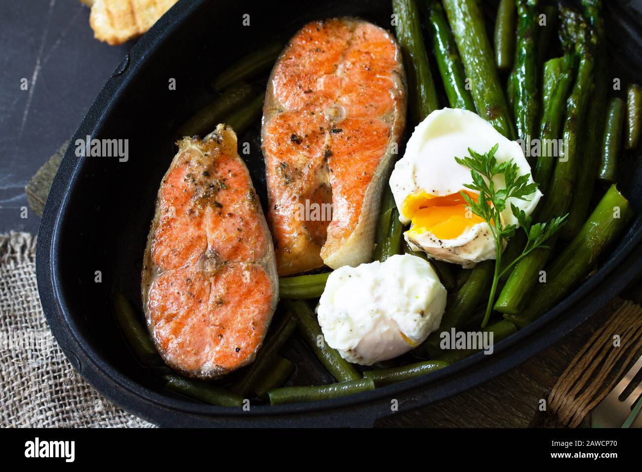 Green asparagus, grilled salmon and poached eggs. Healthy food on rustic wooden background. Stock Photo