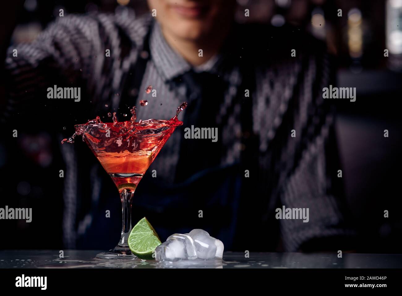 Barman is preparing red cocktail in martini glass. Splashes, dark background. Stock Photo