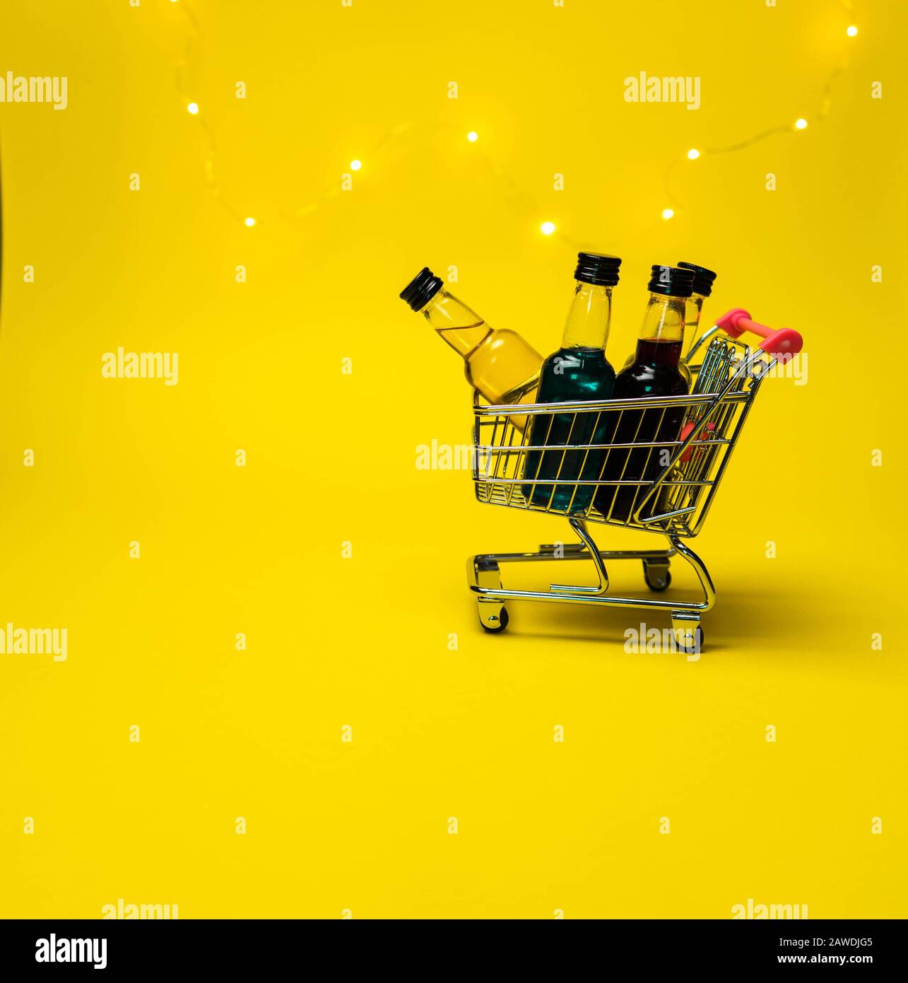 mini shopping cart full of small alcohol bottles yellow background back Stock Photo