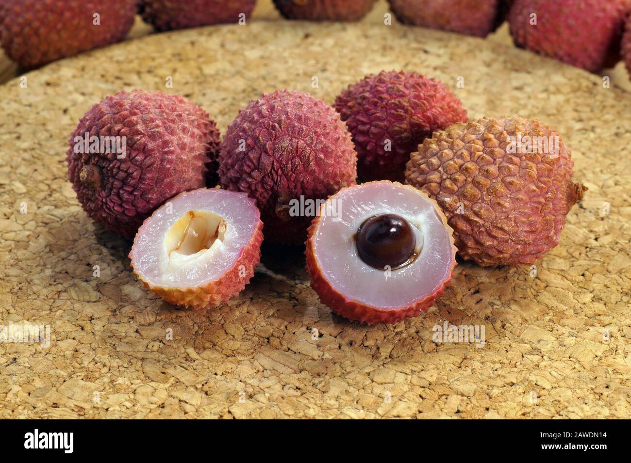 For dessert. A view of the cross-section of a lychee fruit with seed, next to whole fruits. Stock Photo