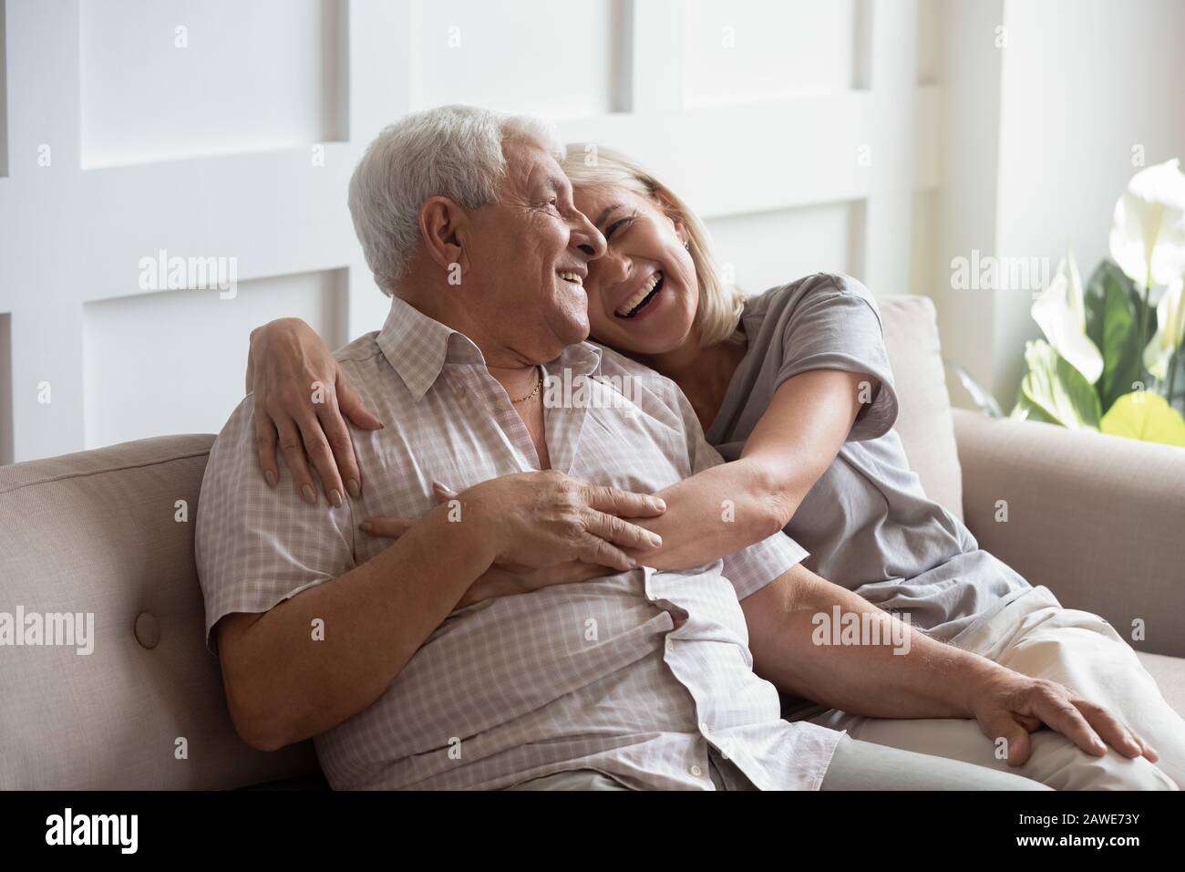 Happy elderly husband and wife relax hugging on couch Stock Photo