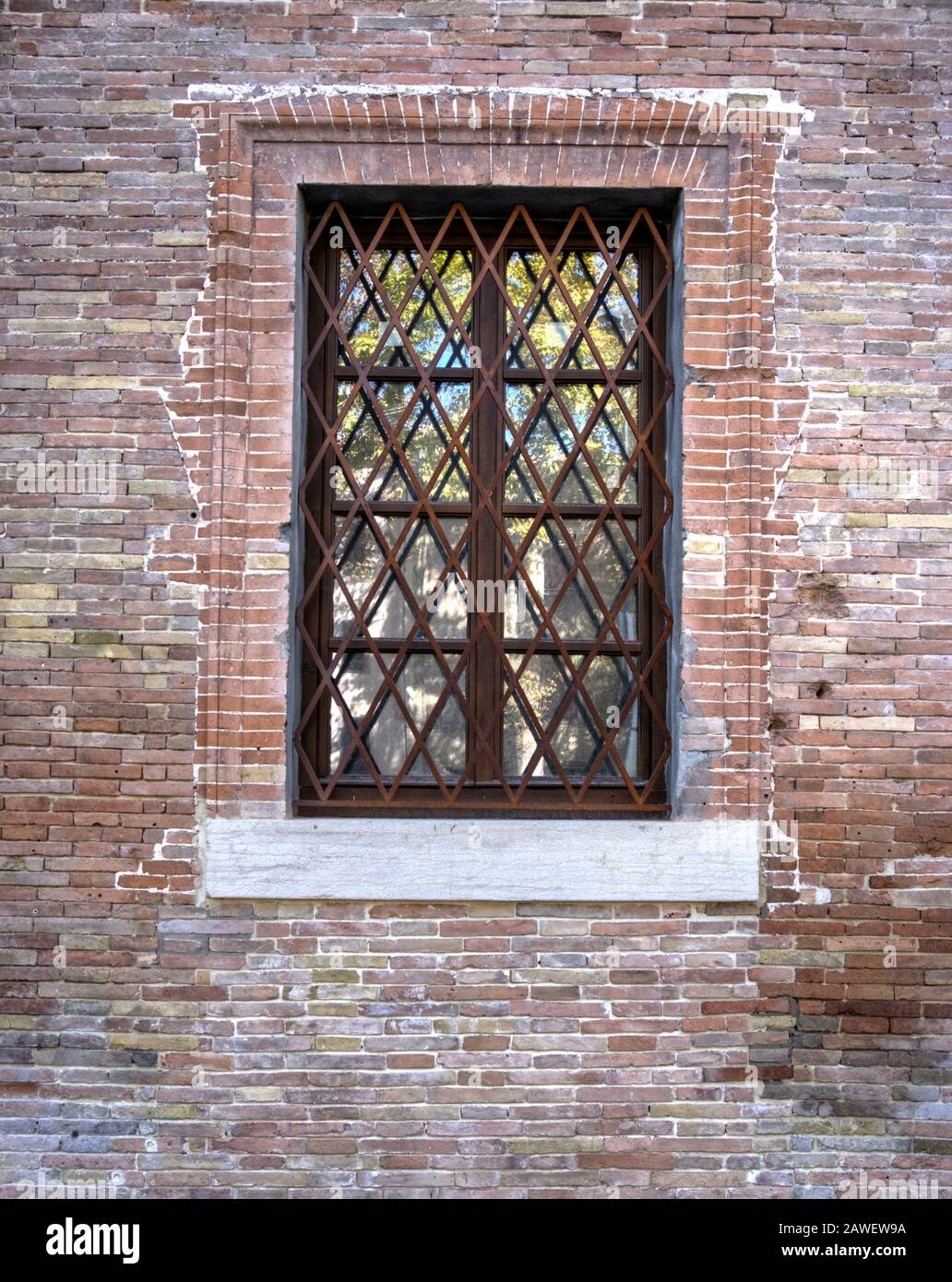 Window with grating in old masonry brick wall with repaired brick work Stock Photo