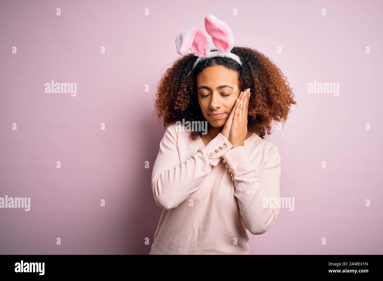 Young african american woman with afro hair wearing bunny ears over pink  background sleeping tired dreaming and posing with hands together while  smili Stock Photo - Alamy