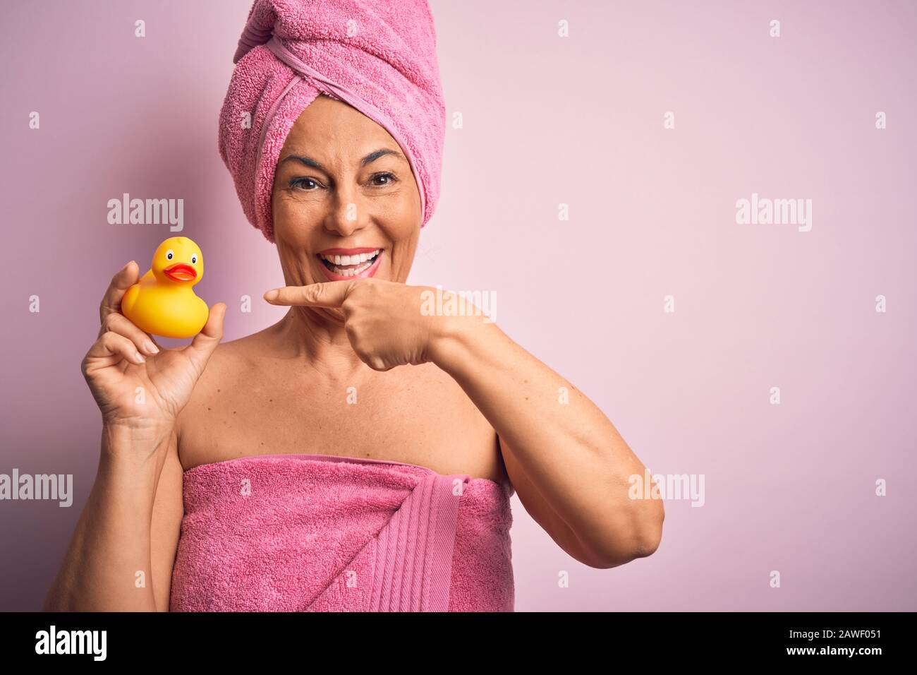 Middle age woman wearing pink bath towel from beauty body care holding rubber yellow duck very happy pointing with hand and finger Stock Photo