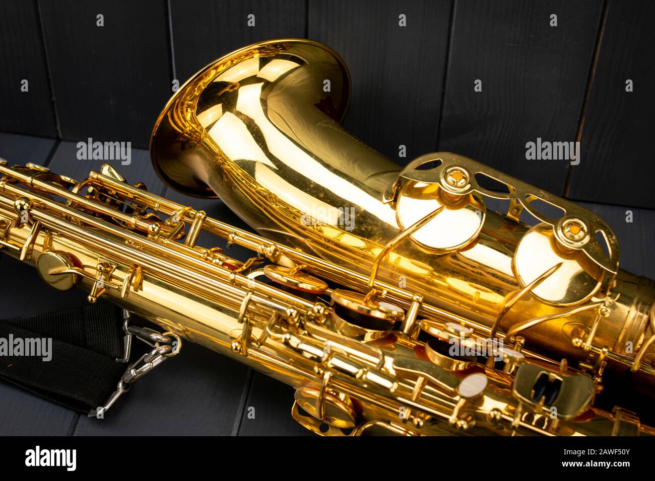 Bell and body of a golden and shiny saxophone with strap on gray wooden background Stock Photo