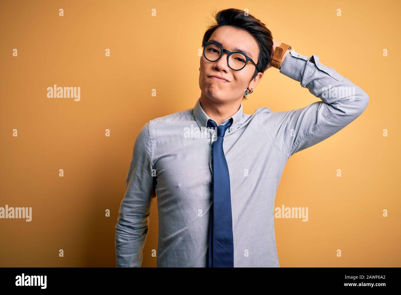 Young handsome chinese businessman wearing glasses and tie over yellow background confuse and wonder about question. Uncertain with doubt, thinking wi Stock Photo