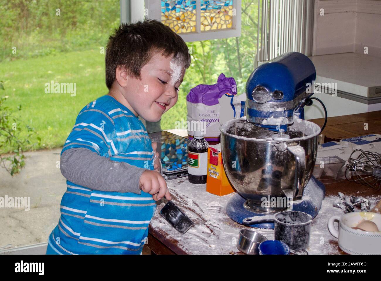 A cute little boy covered in flour makes cookies in grandma's kitchen Stock Photo