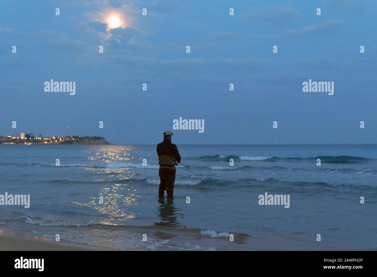 Fisherman standing at the seashore hooks a fish. Sportsman holds a fishing rod and reel in a hooked fish. Spin Fishing hobby catching a fish at the be Stock Photo