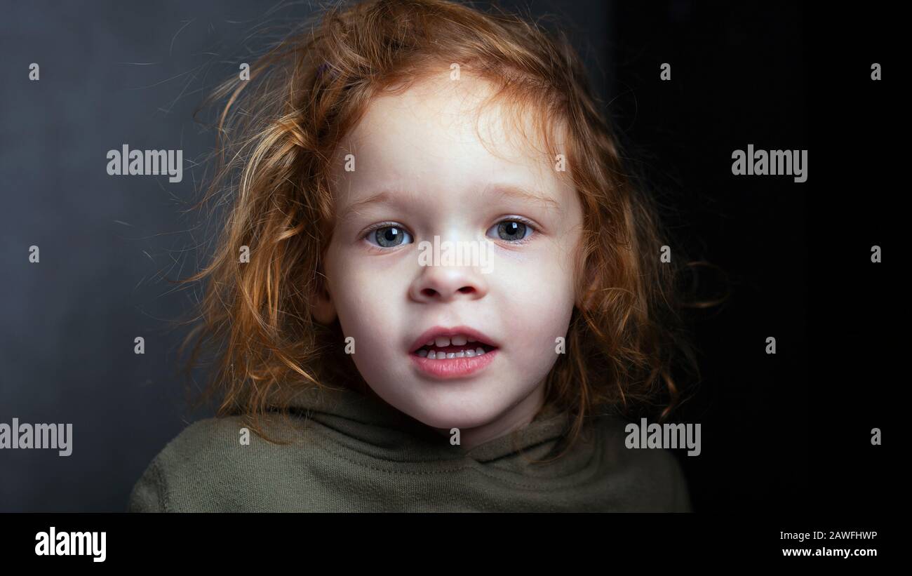 pretty red-haired little girl, cute child portrait on gray background. Stock Photo