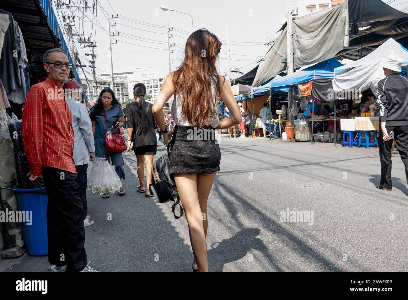 Woman wearing a mini skirt attracting a furtive glance from male admirer; Thailand street Stock Photo