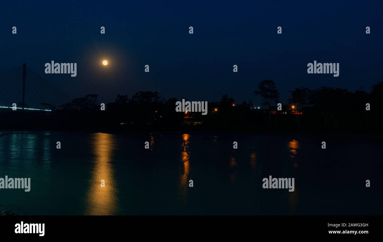 Night view with yellow moon of the bridge over the Aguarico river next to the city of Lago Agrio with lights of houses lit among the trees in the Ecua Stock Photo