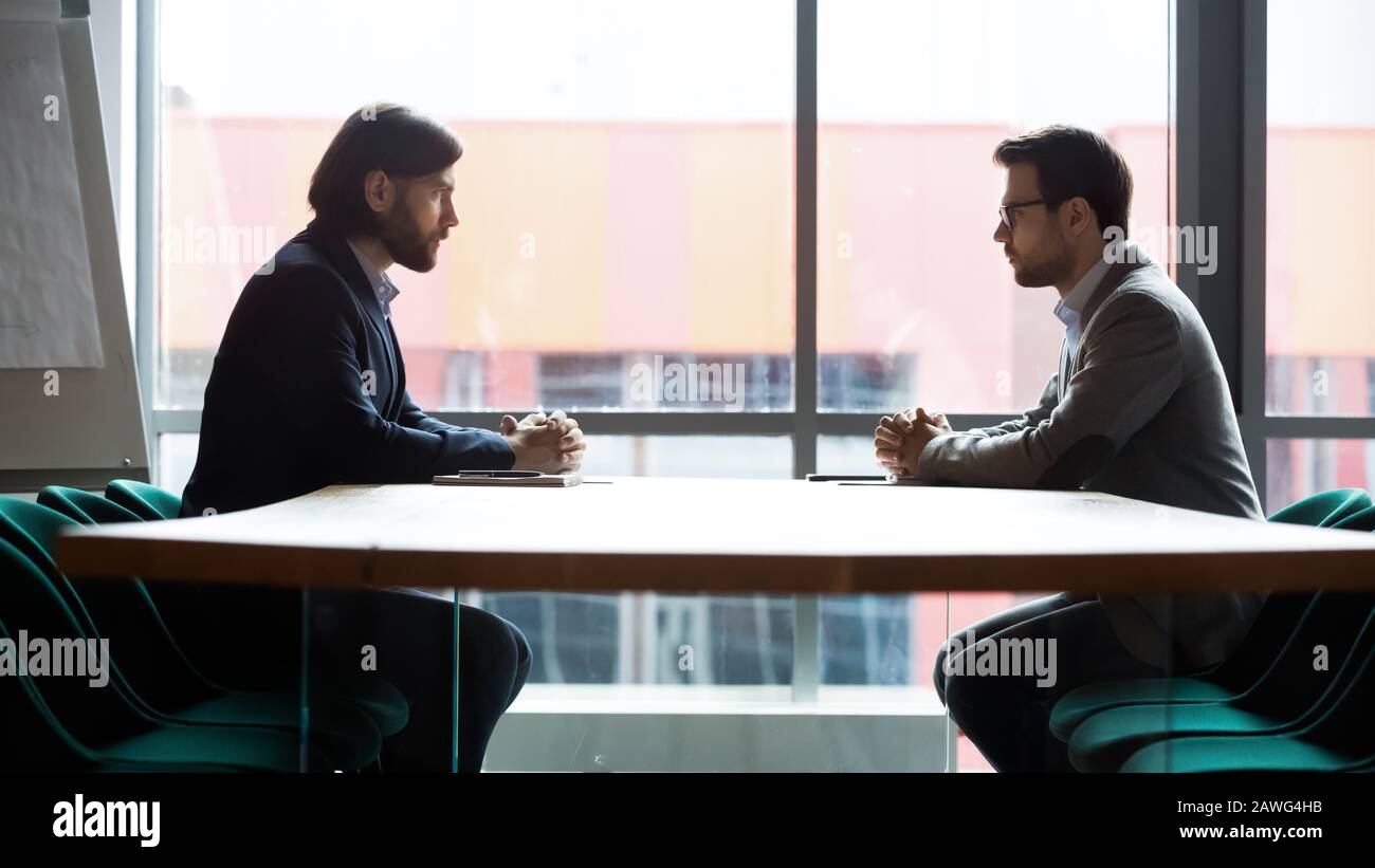 Two businessmen sitting opposite at table, confrontation and negotiation Stock Photo
