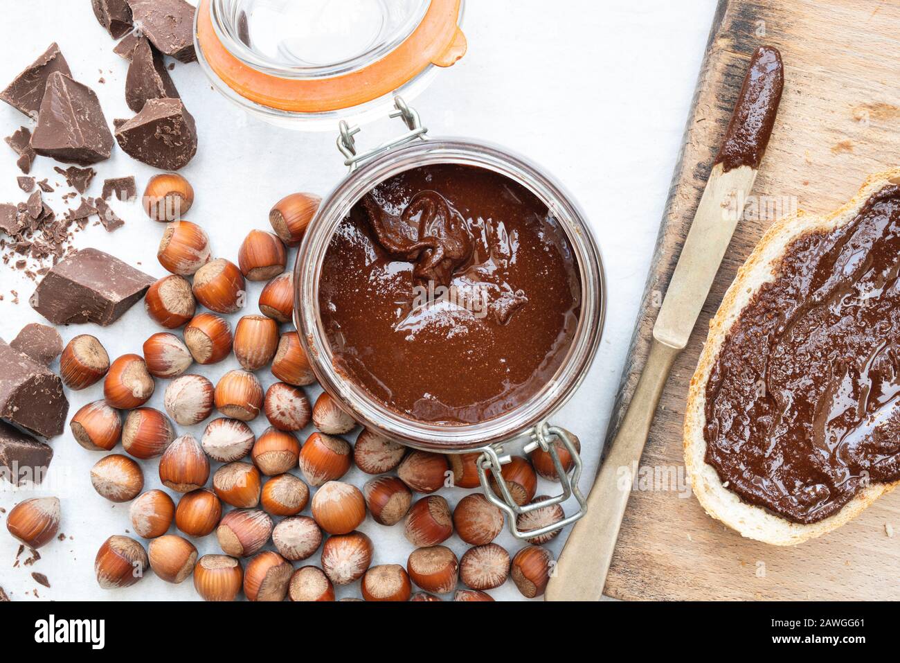 Homemade vegan hazelnut chocolate spread on sourdough bread and in a kilner jar, with unshelled hazelnuts and chunks of dark chocolate Stock Photo