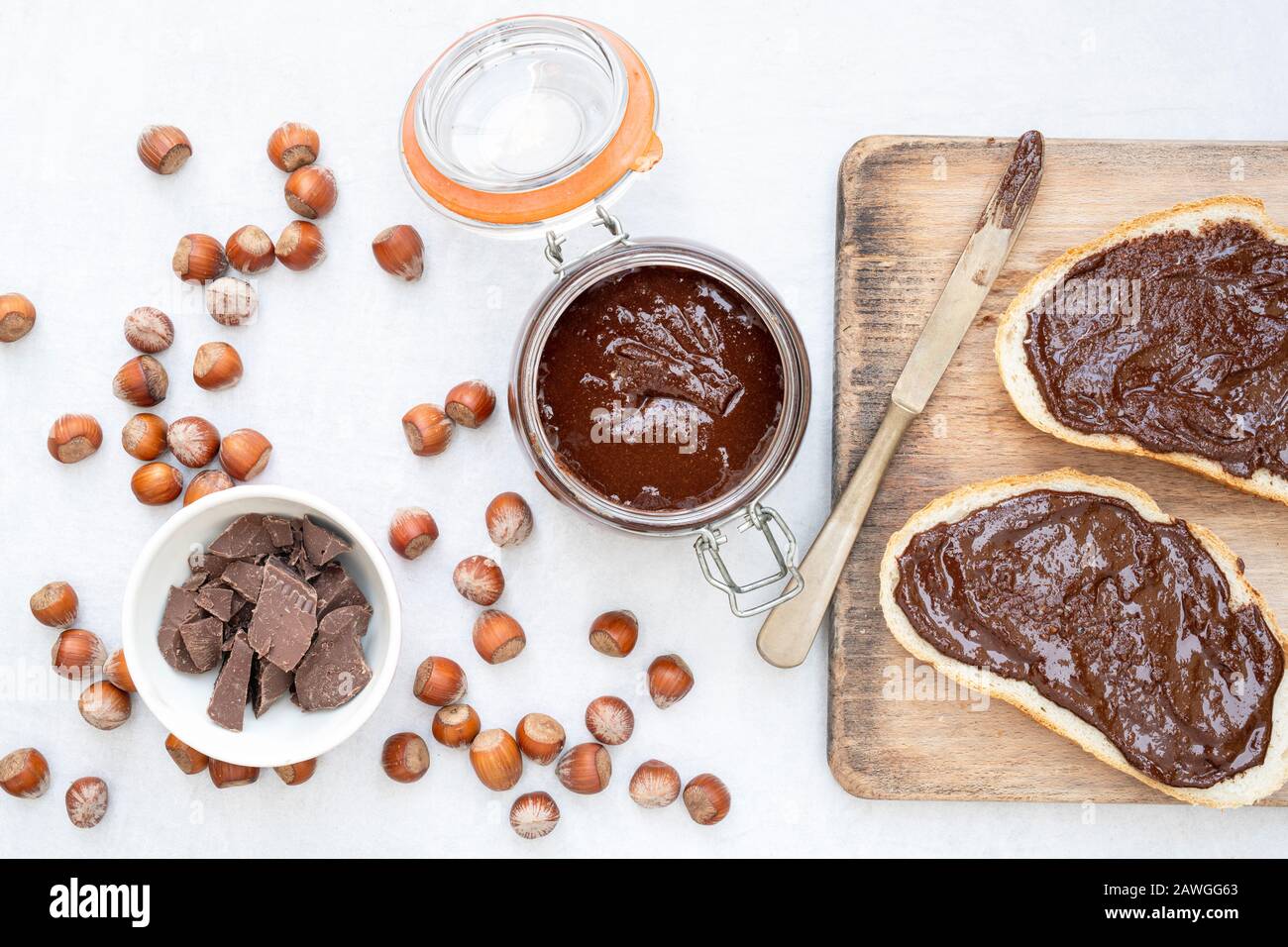 Homemade vegan hazelnut chocolate spread on sourdough bread and in a kilner jar, with unshelled hazelnuts and chunks of dark chocolate Stock Photo