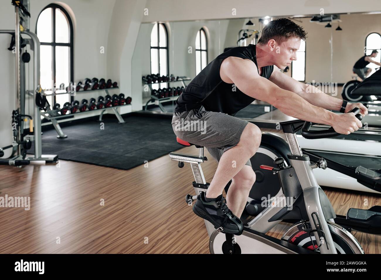 Strong fit young man exercising on stationary bike in gym Stock Photo