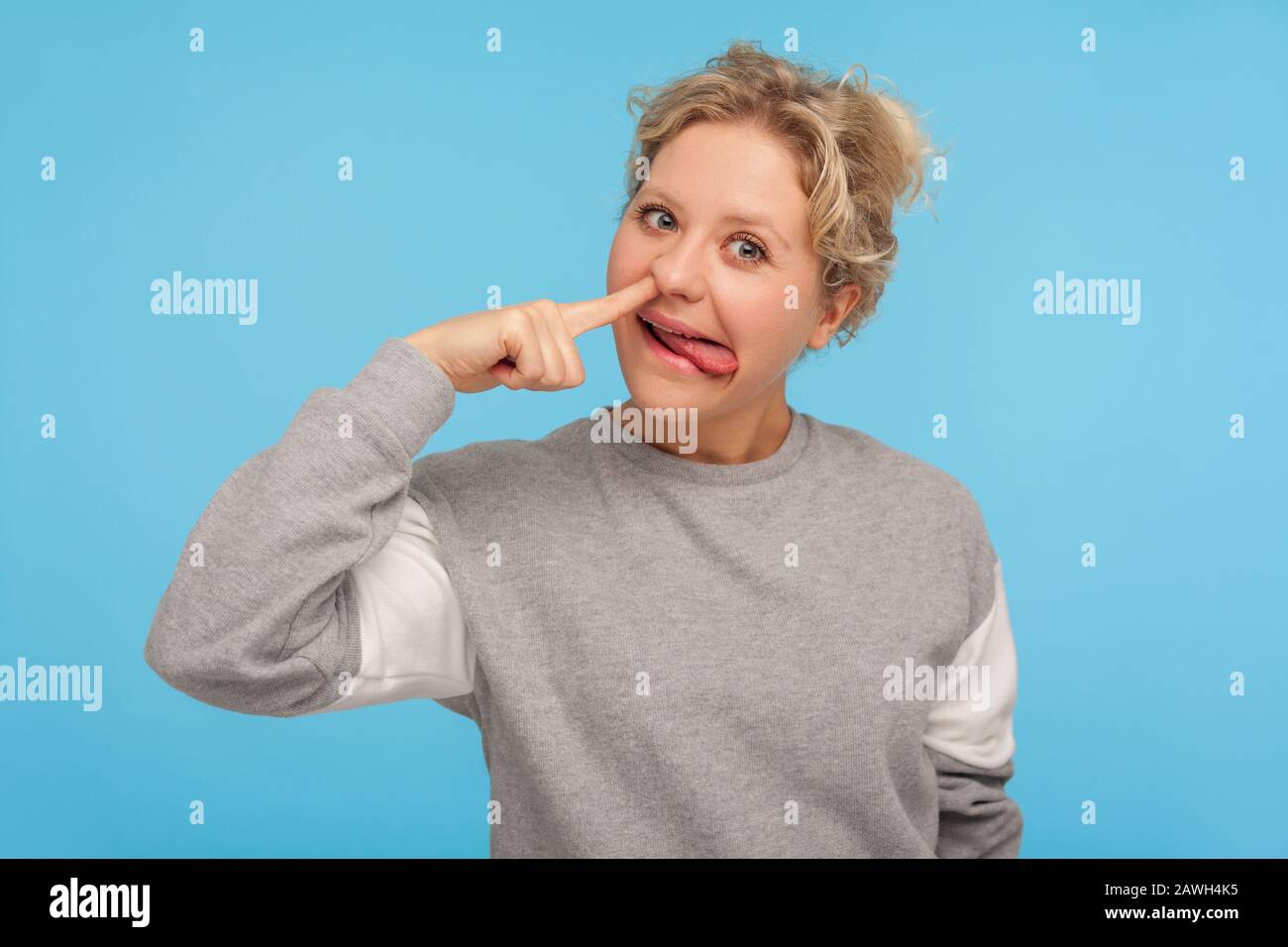 Funny cheerful woman with short hair in casual sweatshirt picking nose with stupid silly face, pulling out boogers, bad manners concept, misconduct . Stock Photo