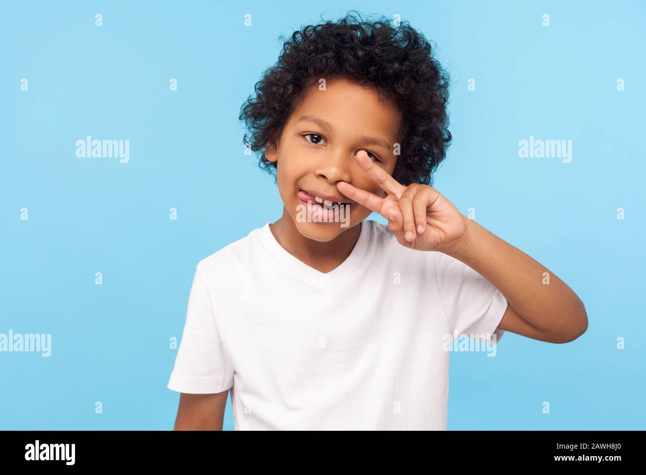 Portrait of cheerful carefree little boy with curly hair in T-shirt picking nose and sticking out tongue with happy face, having fun, bad manners conc Stock Photo