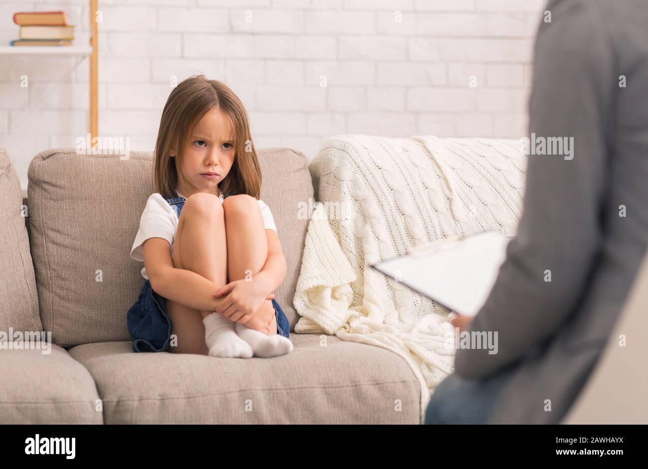 Concerned Little Girl Sitting Alone At Therapy Session With Children Psychologist Stock Photo
