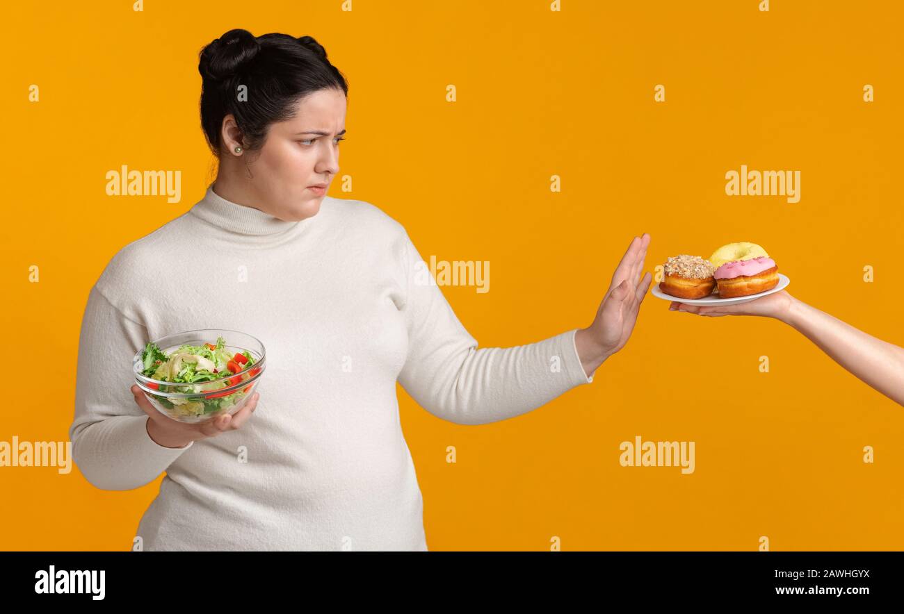 Plump girl refusing junk food, holding bowl with fresh vegetable salad ...
