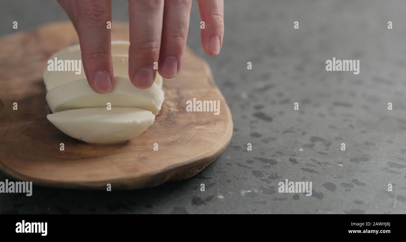 man slicing fresh mozzarella cheese on olive wood board, wide photo